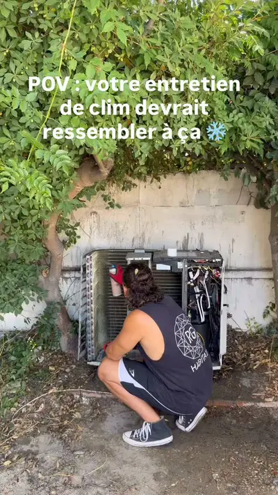 Technicien accroupi devant une unité extérieure de climatisation ouverte pour son entretien