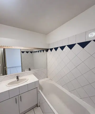 Salle de bain avant travaux : baignoire, meuble lavabo et faïence blanche à frise bleue